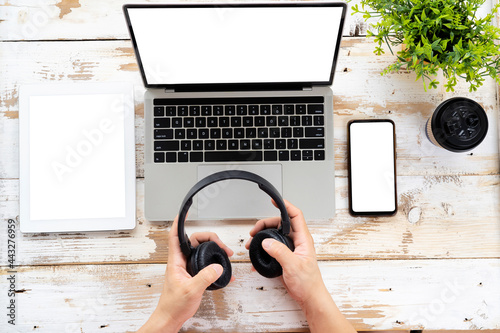 Man holding headphones over wooden table with Laptop, smartphone, tablet blank white background
