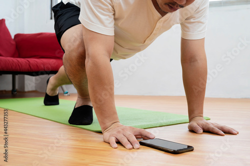 Muscular Athletic Fit Man in T-shirt and Shorts is Doing Mountain Climber Exercises While Using a Stopwatch on His Phone.