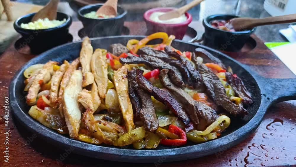 Beef and chicken mix Fajitas with colorful vegetables in black plate. Traditional mexican fajitas on dark sizzling background Beef and chicken mix Fajitas with colorful vegetables in black plate. Traditional mexican fajitas on dark sizzling background
