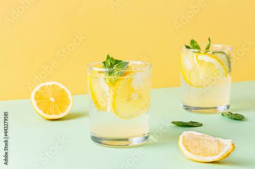 Fruit water with lemon and mint leaves on combined yellow and green background. Two glasses of cool carbonated cocktail with citrus.