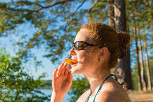 Red-haired girl in a swimsuit and sunglasses eating chips outdoors