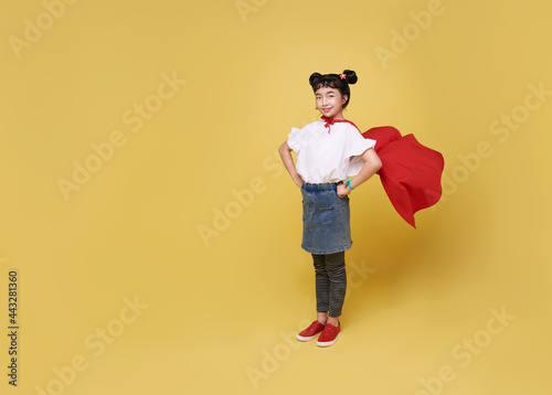 Little child asian girl plays superhero on yellow background studio shot. Girl power hero concept.