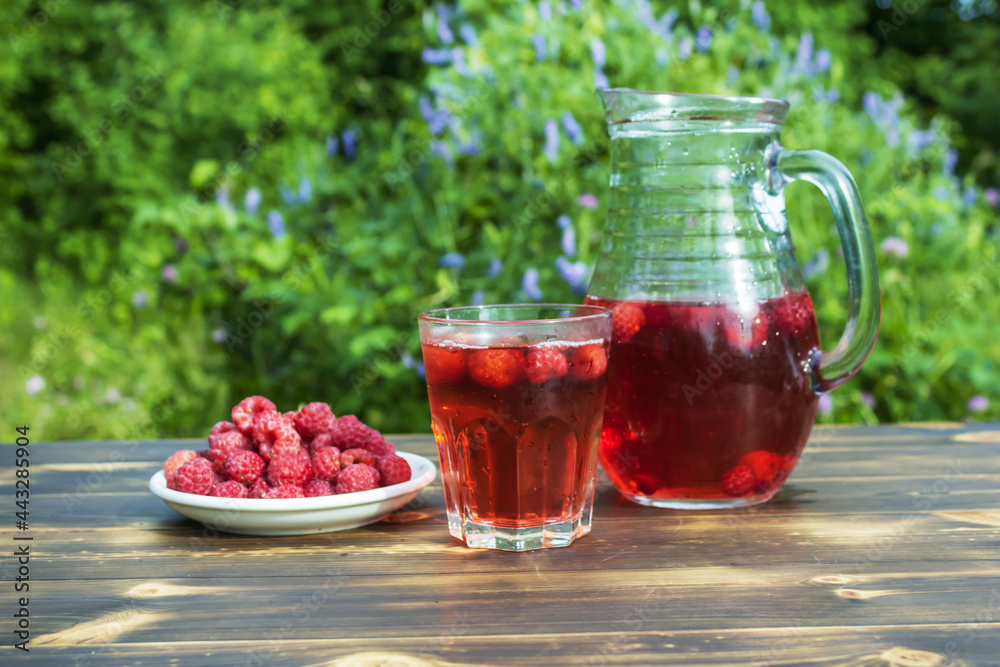 A jug and a mug with compote and a plate with fresh raspberries on a wooden table. A jug and a mug with compote and a plate with fresh raspberries on a wooden table.