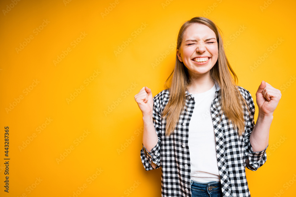 Happy girl in a plaid shirt rejoices in victory clenching her hands into fists, opening her mouth and closing her eyes Happy girl in a plaid shirt rejoices in victory clenching her hands into fists, opening her mouth and closing her eyes