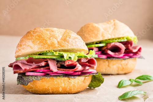 Ready-to-eat hamburger with pastrami, cucumber, radish and herb on craft paper. American fast food. Close-up