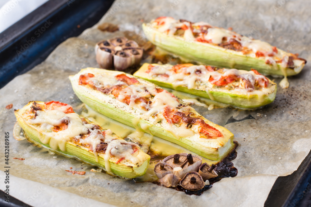 Ready-to-eat baked zucchini halves stuffed with cheese and tomato on baking paper on a baking sheet. Vegetable dishes, healthy food