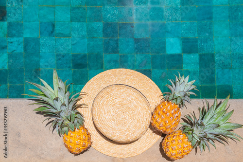 Straw hat and three pineapples by the refreshing pool, viewed from above.