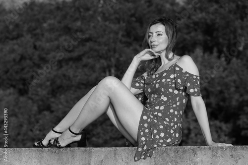 Beautiful woman in summer dress sitting on concrete fence in black and white