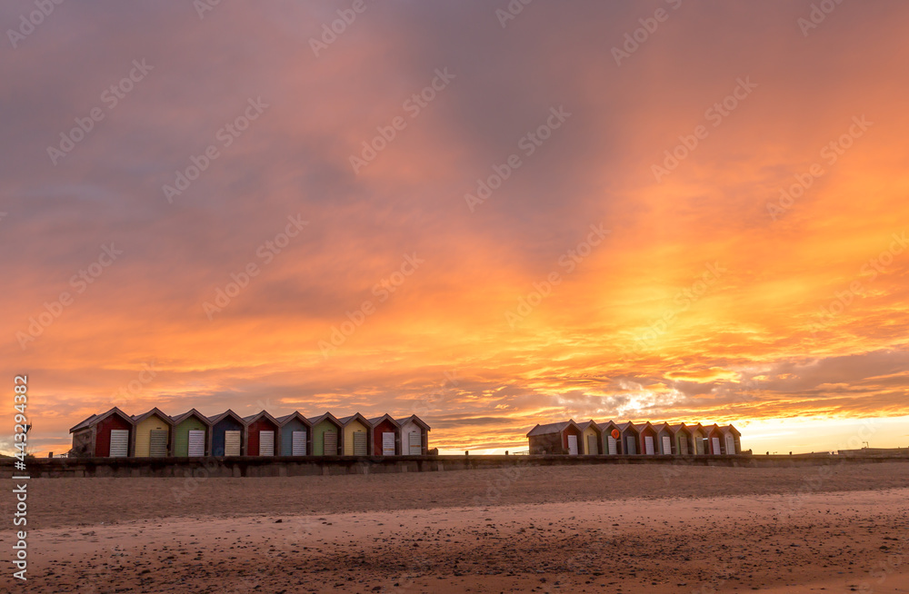 Fototapeta premium The vibrant and colorful beach huts by the promenade overlooking Blyth beach with a lovely sunset in Northumberland, England