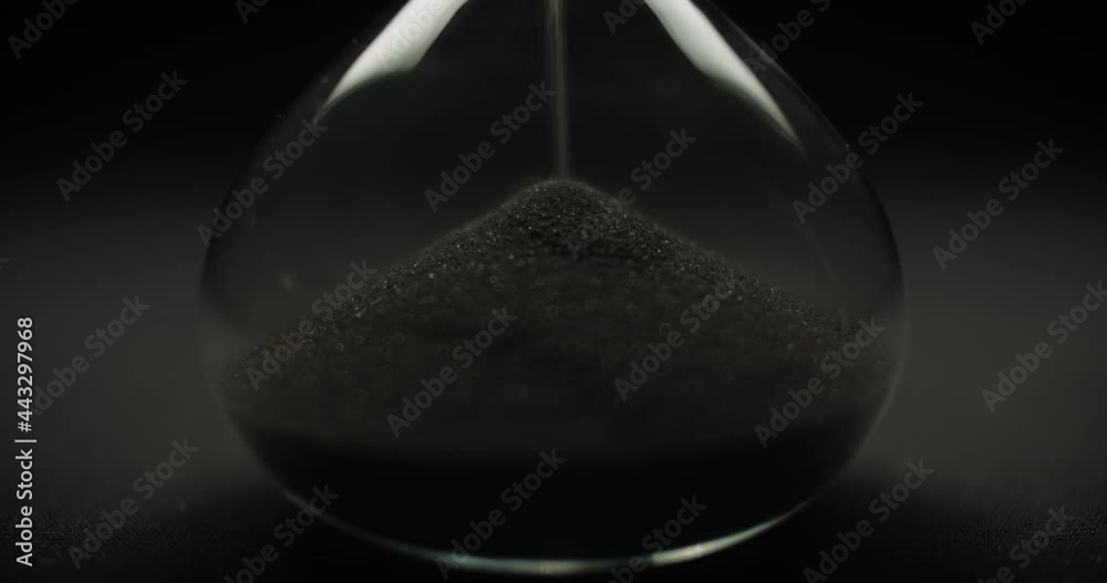 Macro shot of black sand falling in reverse inside a transparent sand glass. Reverse time concept. 