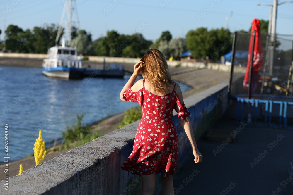 Slender woman in red dress walking by embankment
