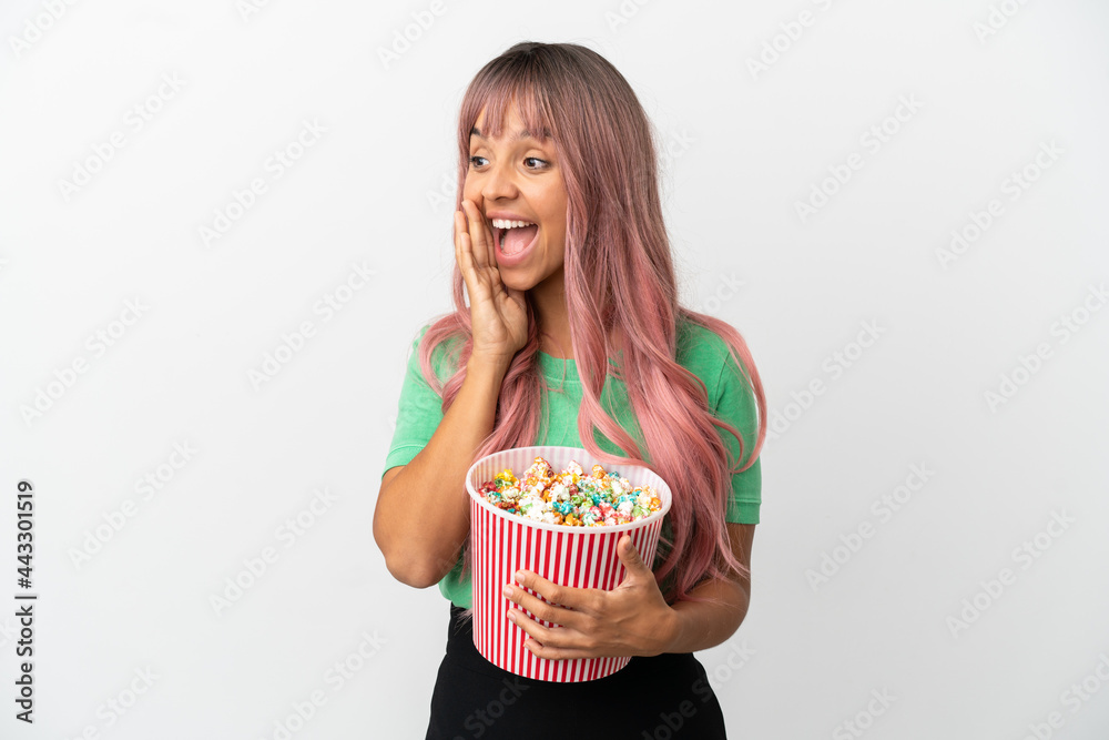Young mixed race woman with pink hair eating popcorn isolated on white background shouting with mouth wide open to the side