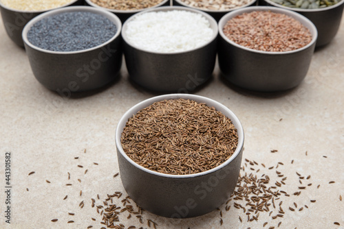 Caraway seeds. Cup with caraway seeds on a background of various seeds in black containers on a marble table top