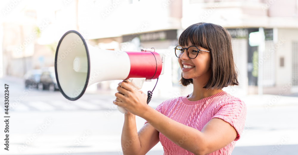 Young brunette woman in the city shouting through a megaphone to announce something Young brunette woman in the city shouting through a megaphone to announce something