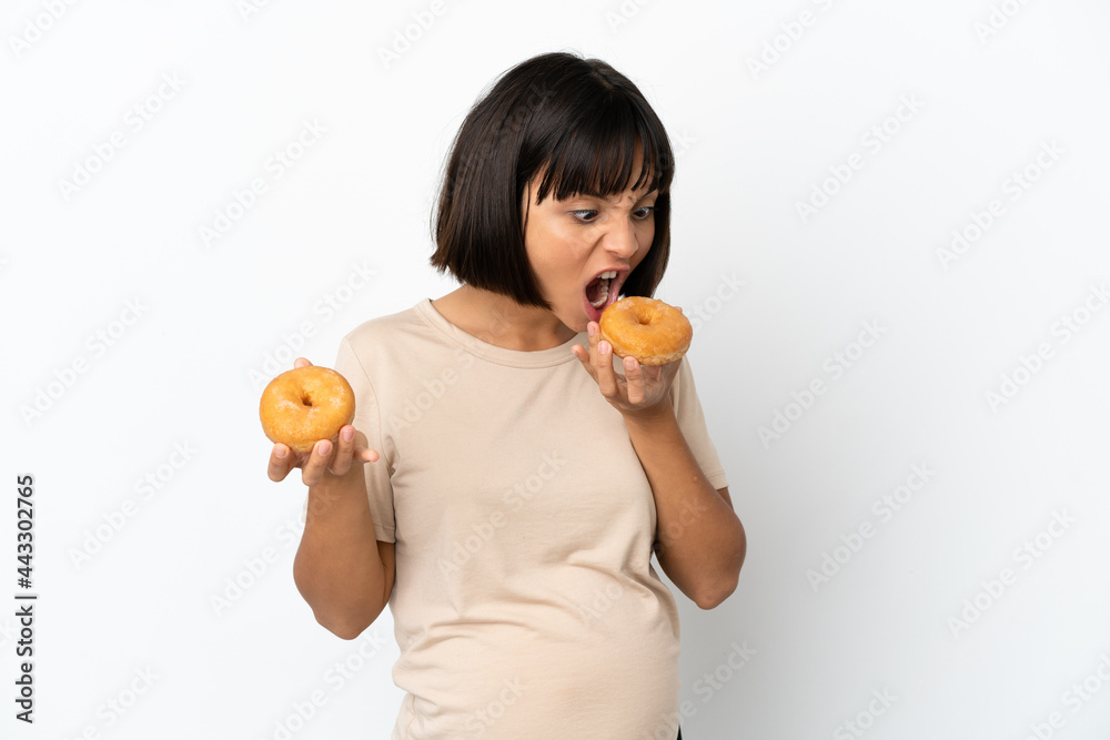 Young mixed race pregnant woman isolated on white background eating a donut Young mixed race pregnant woman isolated on white background eating a donut
