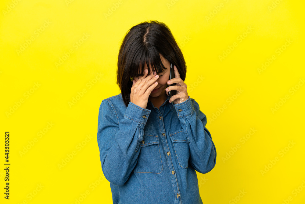 Pregnant woman using mobile phone isolated on yellow background with tired and sick expression Pregnant woman using mobile phone isolated on yellow background with tired and sick expression