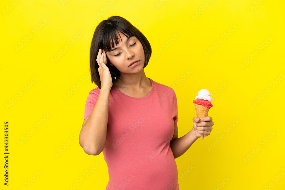 Pregnant woman holding a cornet ice cream isolated on yellow background with headache Pregnant woman holding a cornet ice cream isolated on yellow background with headache