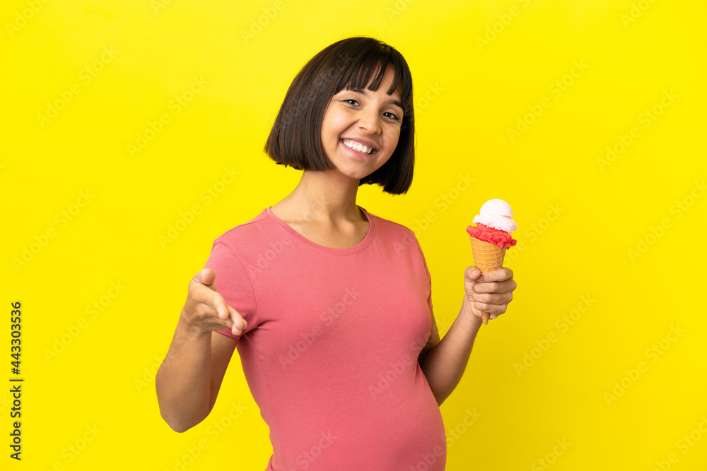 Pregnant woman holding a cornet ice cream isolated on yellow background shaking hands for closing a good deal Pregnant woman holding a cornet ice cream isolated on yellow background shaking hands for closing a good deal
