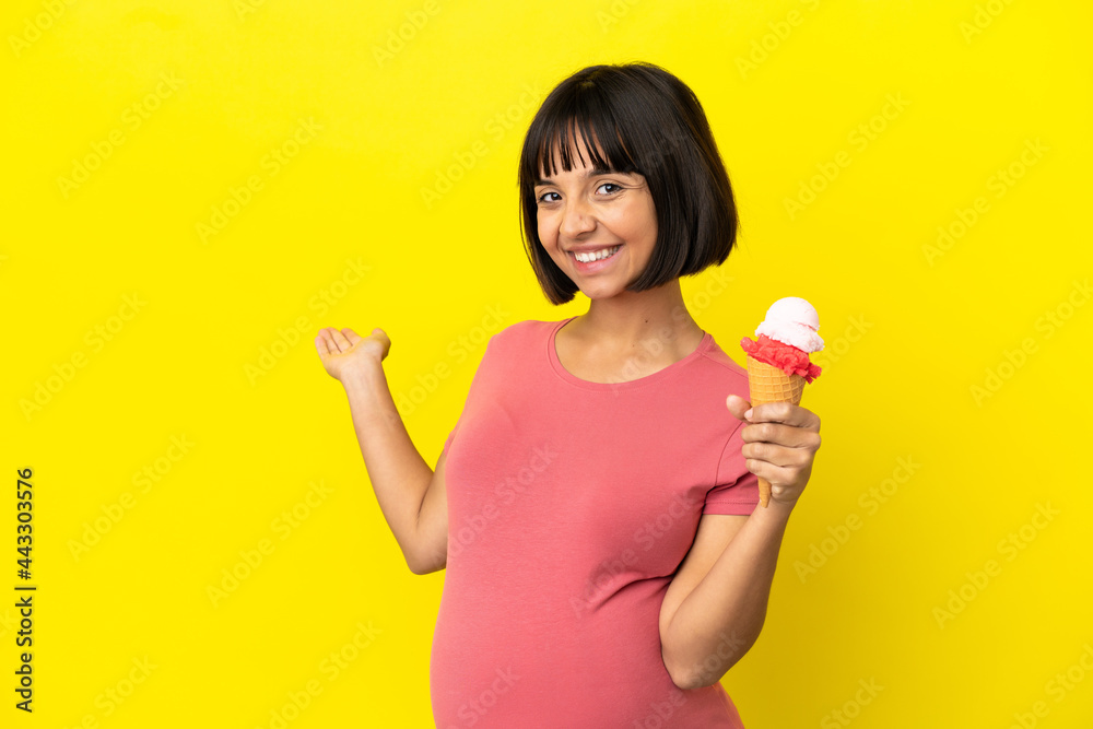 Pregnant woman holding a cornet ice cream isolated on yellow background extending hands to the side for inviting to come Pregnant woman holding a cornet ice cream isolated on yellow background extending hands to the side for inviting to come