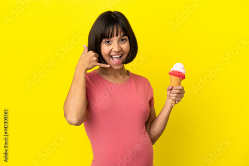 Pregnant woman holding a cornet ice cream isolated on yellow background making phone gesture. Call me back sign © luismolinero