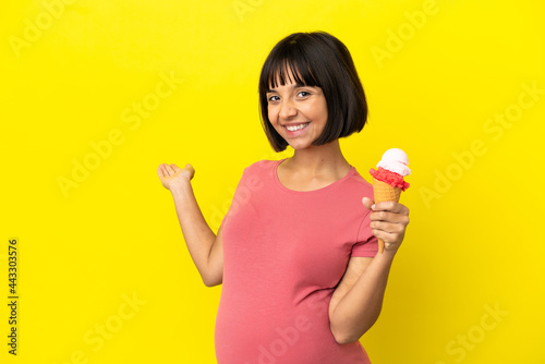Pregnant woman holding a cornet ice cream isolated on yellow background extending hands to the side for inviting to come © luismolinero