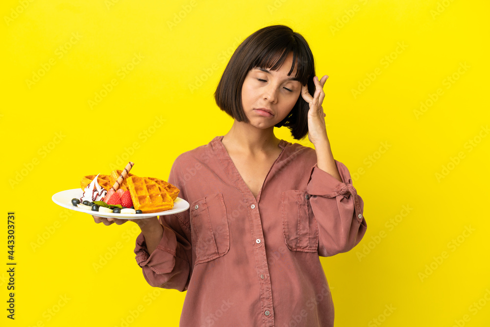 Pregnant woman holding waffles isolated on yellow background with headache Pregnant woman holding waffles isolated on yellow background with headache