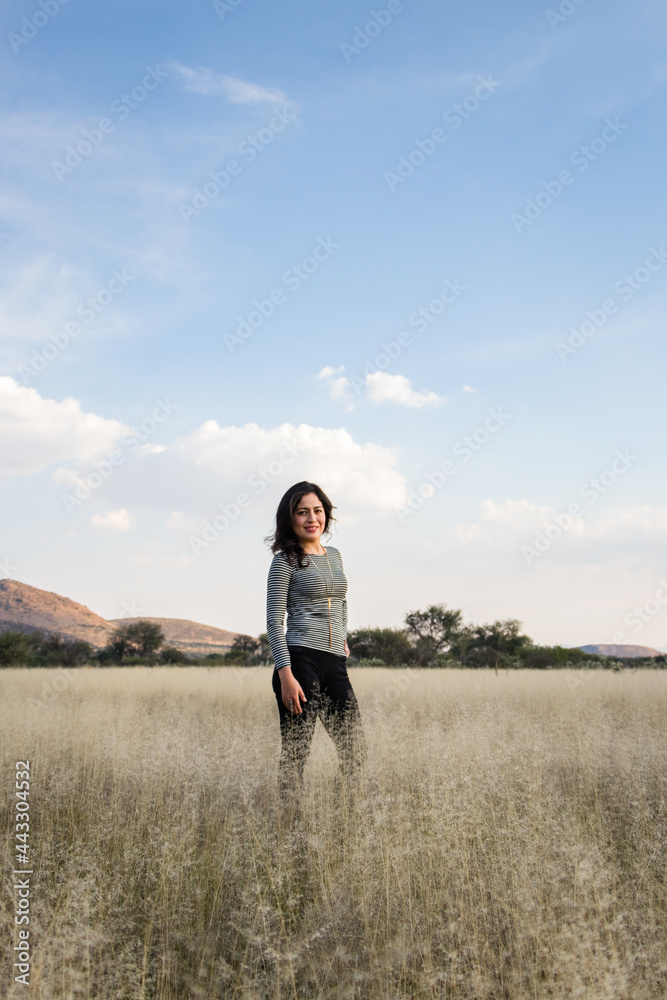 Young adult Mexican woman standing in a dry grassy meadow looking at the camera