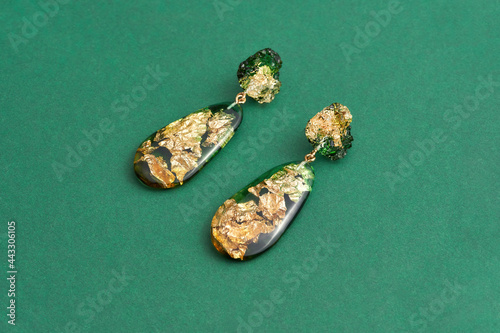 Close up shot of dangle earrings made of epoxy resin with golden foil inside isolated over green background photo