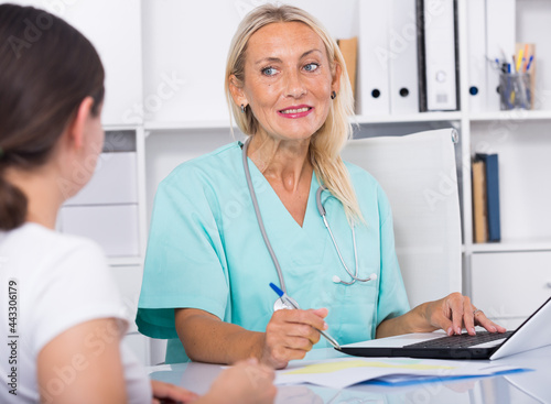 Portrait of mature female doctor listening to patient complaints at clinic