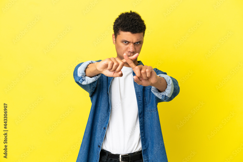 Young African American man isolated on yellow background making stop gesture with her hand to stop an act Young African American man isolated on yellow background making stop gesture with her hand to stop an act
