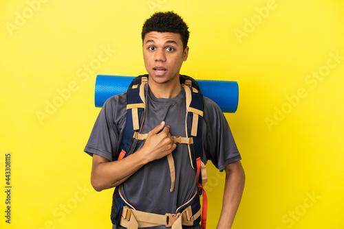 Young mountaineer African American man with a big backpack isolated on yellow background with surprise facial expression