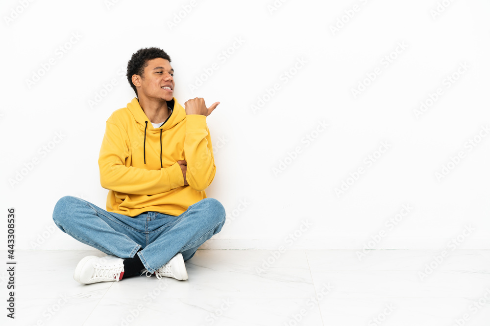 Young African American man sitting on the floor isolated on white background pointing to the side to present a product Young African American man sitting on the floor isolated on white background pointing to the side to present a product