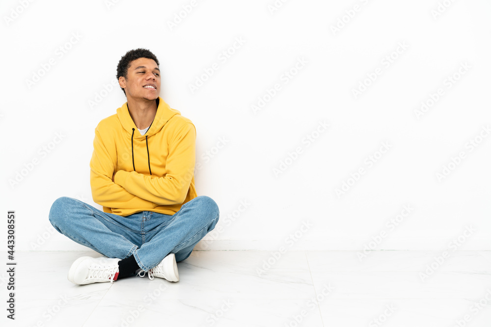 Young African American man sitting on the floor isolated on white background with arms crossed and happy Young African American man sitting on the floor isolated on white background with arms crossed and happy