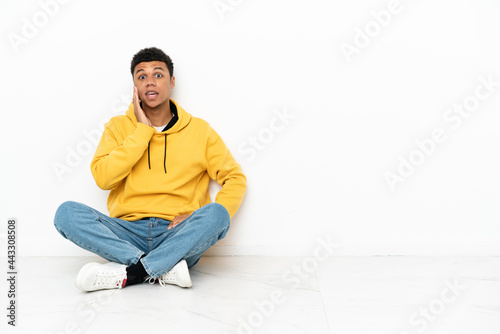 Young African American man sitting on the floor isolated on white background with surprise and shocked facial expression © luismolinero