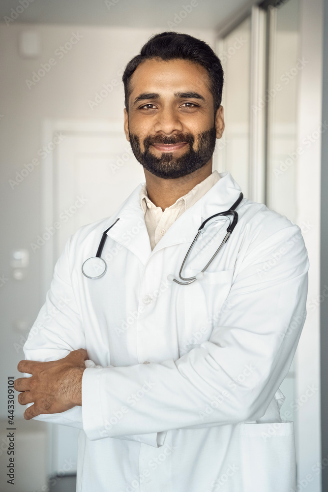 Vertical portrait of smiling young indian male doctor in medical robe uniform Vertical portrait of smiling young indian male doctor in medical robe uniform