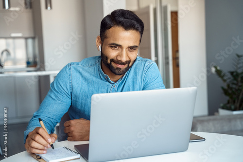 Portrait of young adult indian man wearing earphones looking at laptop screen