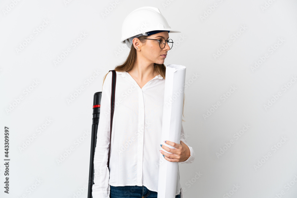 Young Lithuanian architect woman with helmet and holding blueprints isolated on white background looking to the side Young Lithuanian architect woman with helmet and holding blueprints isolated on white background looking to the side