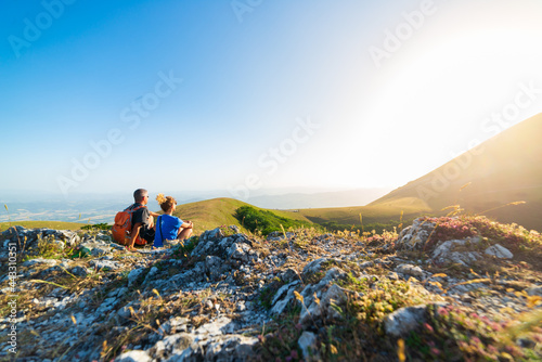 Man and woman hiking in the mountains of Umbria region, Monte Cucco, Appennino, Italy. Couple watching sunset together on mountain top. Summer outdoors activity. © fabio lamanna