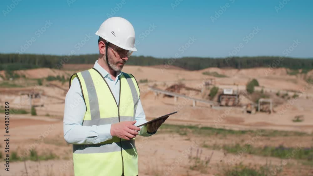Handsome sand quarry worker engineer, male caucasian foreman in safety wear and hardhat working with digital tablet computer and looking at camera. Bearded industrial worker, mining project specialist Handsome sand quarry worker engineer, male caucasian foreman in safety wear and hardhat working with digital tablet computer and looking at camera. Bearded industrial worker, mining project specialist