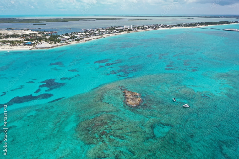 Aerial view of boats anchored near coral rocks with North Bimini coast in background on sunny summer afternoon.