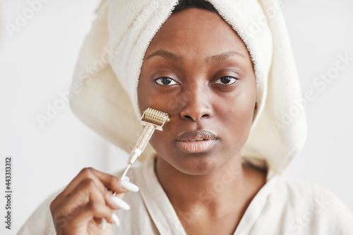 Front view portrait of beautiful African-American woman doing microdermal face massage while at home and looking at camera, copy space photo