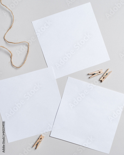 Three blank white sheets of square format paper, rope, and clothespins. Blank paper lies on a light table. Mock up poster with place for your design. Top view.