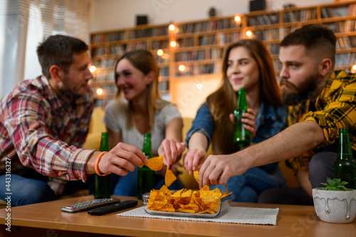 Group of friends on a house party drinking beer and eating nachos