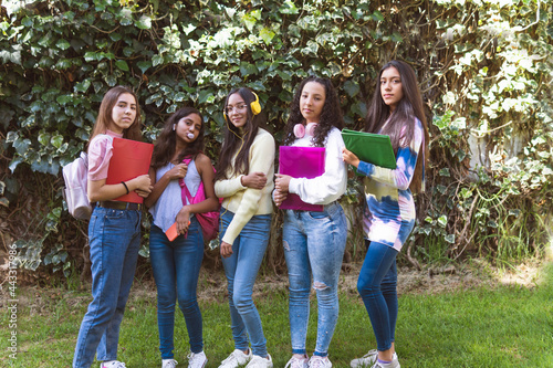 Portrait of teenage girls with their notebooks and backpacks looking at camera in a green garden