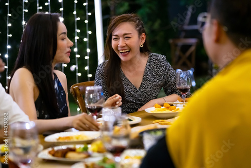 Group of diversity Asian millennial people friends enjoy outdoor garden dinner party eating food and drinking wine with talking together. Reunion friendship meeting celebration and night life concept.