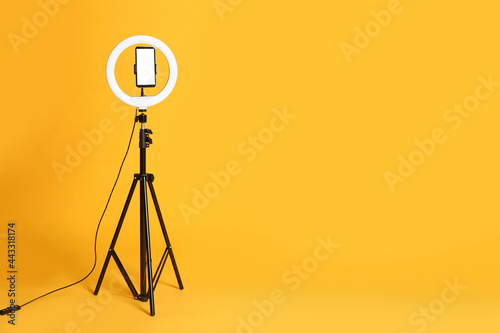 Modern tripod with ring light and smartphone on yellow background. Space for text