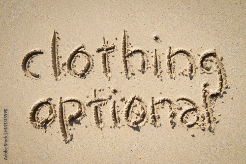 Clothing optional nudist message handwritten in simple text on smooth sand beach 