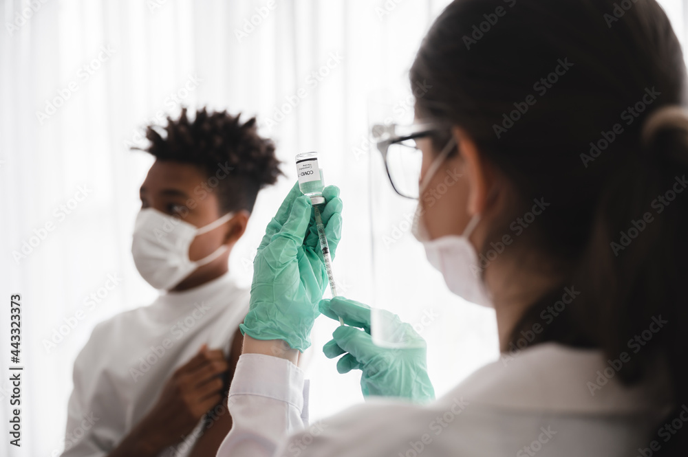 Female doctor or nurse wearing mask, gloves, and visor preparing to vaccinate coronavirus 19 to immunize African-American men.Concepts to prevent the spread of COVID-19. Female doctor or nurse wearing mask, gloves, and visor preparing to vaccinate coronavirus 19 to immunize African-American men.Concepts to prevent the spread of COVID-19.