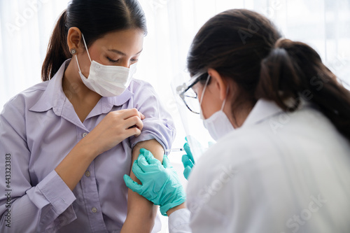 A female doctor or nurse wearing a mask, glove, and face shield are injecting the coronavirus 19 vaccine on the shoulder of the woman to immunize. Concept of preventing the spread of COVID-19.
