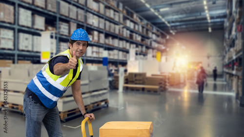 Warehouse  worker pulling a pallet truck and taking or upload package box to shelf in large warehouse. Active caucasian man showing thump up and looking at camera with smiling. © feeling lucky